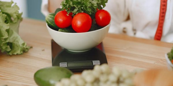 Colorful fresh vegetables including tomatoes and cucumbers on a kitchen scale for healthy eating.