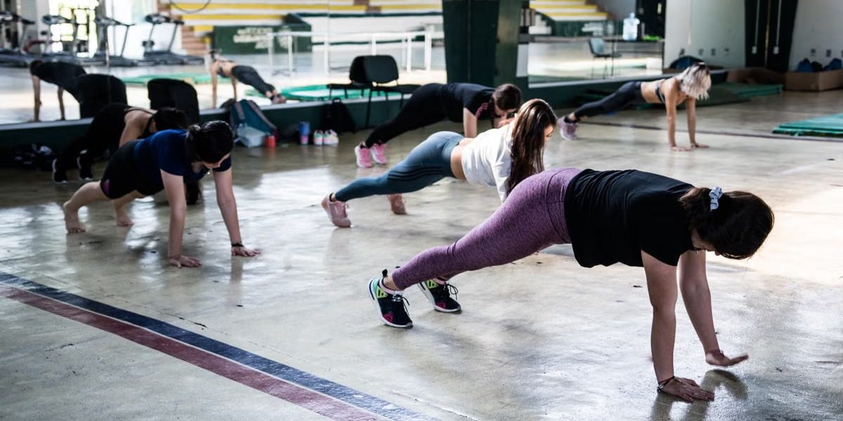 Group of women doing push-ups in a gym reflecting in a mirror.
